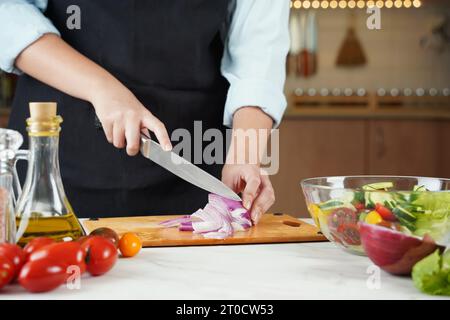 La femme en train de faire de la salade de légumes. Gros plan des mains coupant des oignons rouges sur la table en bois Banque D'Images