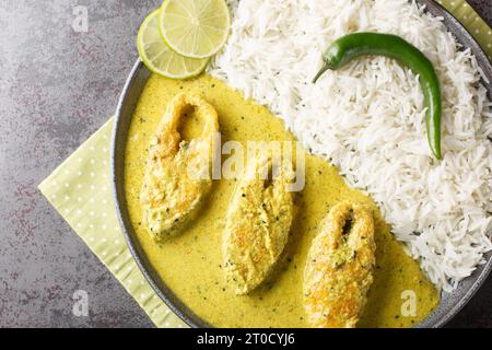 Poisson Hilsa à la sauce moutarde ou Shorshe Ilish servi avec du riz blanc en gros plan sur l'assiette sur la table. Vue de dessus horizontale Banque D'Images