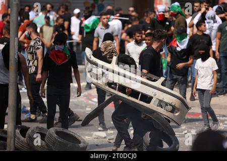 Huwara, Territoires palestiniens. 06 octobre 2023. Des Palestiniens se mettent à couvert derrière une partie d’une voiture lors d’affrontements entre les forces israéliennes et les Palestiniens à la suite des funérailles de Labib Damidi (19 ans), abattu lors d’une attaque de nuit dans le village de Huwara, dans le village de Cisjordanie occupé par Israël. Crédit : Ilia Yefimovich/dpa/Alamy Live News Banque D'Images