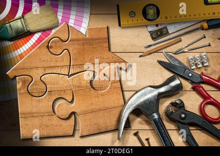 Concept d'amélioration de la maison. Maison en bois faite de pièces de puzzle sur un établi en bois avec de nombreux outils de travail. Banque D'Images