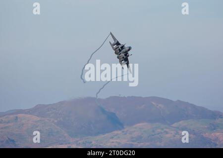 Avion à réaction militaire américain F15 volant sur un vol d'entraînement à travers un ciel bleu avec des collines galloises en arrière-plan Banque D'Images