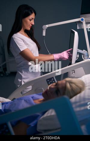 Joli médecin féminin utilise un équipement moderne dans la salle de réveil Banque D'Images