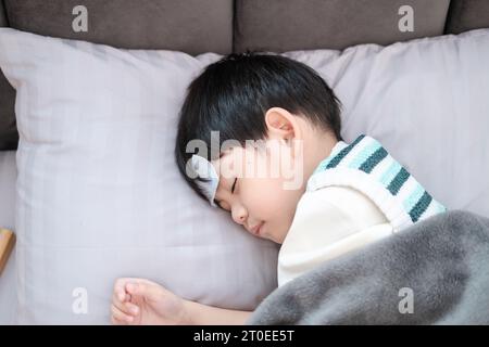 Garçon asiatique elle était malade et avait un patch réduisant la fièvre sur son front. Elle était allongée sur le lit. Banque D'Images