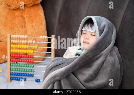 Garçon asiatique couché malade, il avait un patch réduisant la fièvre sur son front et s'est couvert d'une couverture à cause du froid. Banque D'Images