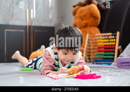Garçon asiatique jouant avec des puzzles sur le lit joyeusement Banque D'Images