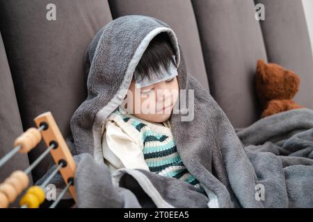 Garçon asiatique couché malade, il avait un patch réduisant la fièvre sur son front et s'est couvert d'une couverture à cause du froid. Banque D'Images