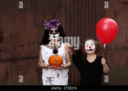 Les filles habillées comme une mariée morte et un clown effrayant dans le contexte d'un garage pendant la nuit d'Halloween Banque D'Images