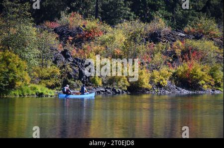 Deux hommes, dans un canoë bleu, pagaient sur Clear Lake en Oregon. L'automne a tourné les buissons bas vers le rouge et l'orange. Banque D'Images