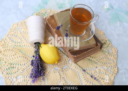 Thé à la lavande dans une tasse en verre, bouquet de lavande dans un livre ouvert, et tranches de citrons mûrs. Concept de loisirs sain et relaxant. Thé apaisant pour un g. Banque D'Images