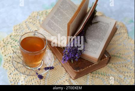 Thé à la lavande dans une tasse en verre, bouquet de lavande dans un livre ouvert, et tranches de citrons mûrs. Concept de loisirs sain et relaxant. Thé apaisant pour un g. Banque D'Images