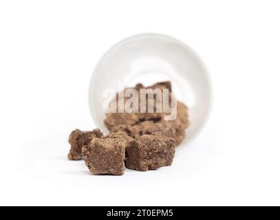 Cubes d'agneau séchés à l'air ou nourriture pour chiens tombant du récipient de stockage défocalisé. Aliments secs isolés pour chiens pour en-cas et gâteries. Agneau brun mono prote Banque D'Images