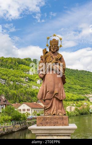 St-Ursanne, Suisse - 15 mai 2023 : Pont d'entrée avec sculpture historique de saint traversant le Doubs dans le village pittoresque de Saint-Ursanne dans le canton du Jura destraire Porrentruy dans la Suisse Banque D'Images