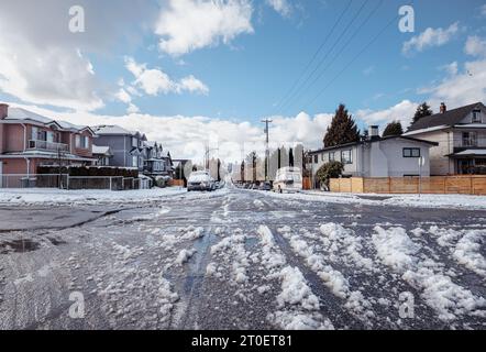 Rue résidentielle glissante après une tempête de neige ou une explosion arctique. Journée ensoleillée avec grande fonte vers le bas sur la rue latérale non labourée avec des voitures garées. East Vancouver avec Banque D'Images