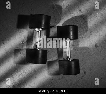 Paire d'haltères isolée sur un sol en béton gris salle de gym. Équipement de fitness moderne pour la musculation, le renforcement de la force, la sculpture des muscles du haut du corps Banque D'Images