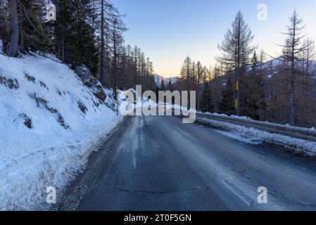 Route alpine sinueuse glacée à travers une forêt enneigée au crépuscule en hiver Banque D'Images