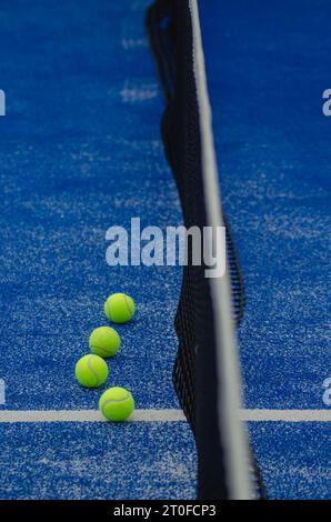 quatre balles de paddle-tennis à côté du filet sur un terrain bleu en gazon artificiel Banque D'Images