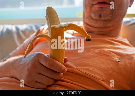 l'homme tient une banane pelée dans ses mains avant de la manger Banque D'Images