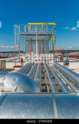 La tuyauterie isolée réfléchissante indique la voie vers un grand condenseur de réfrigération industriel sur le toit d'une installation de stockage frigorifique. Banque D'Images