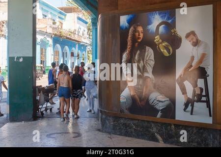 Les Cubains marchent dans un porche de bâtiment dans le centre-ville. Une publicité commerciale est dans le coin. Bâtiments traditionnels de style républicain dans la ba Banque D'Images