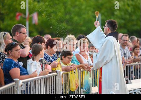 Un prêtre bénit les articles religieux des fidèles après la Messe du soir à Medjugorje. Banque D'Images