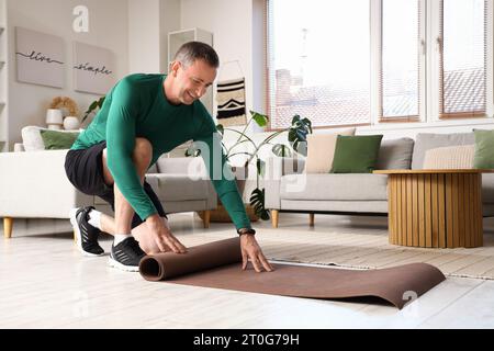 Homme mûr sportif déployant tapis de fitness à la maison Banque D'Images