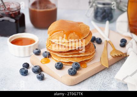 Planche en bois de crêpes savoureuses avec des myrtilles et du sirop d'érable sur fond blanc Banque D'Images