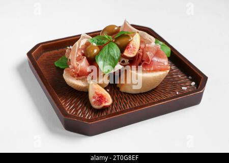 Planche en bois avec des sandwichs savoureux avec prosciutto sur fond blanc Banque D'Images