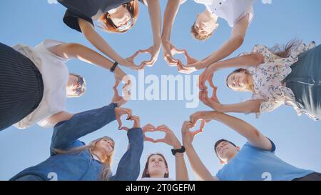 Groupe de sept personnes faisant ensemble un cœur avec leurs doigts et leurs mains - les gens en cricle s'amusent et jouent - vue au sol. Banque D'Images