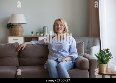 Heureuse blonde mature femme des années 50 reposant sur un canapé doux Banque D'Images