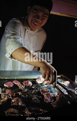 Dans l’Outback, un souriant Chef cuisinant barbecue kangourou – vous ne pouvez pas manger plus australien que cela, dînant sous les étoiles à Uluru. Banque D'Images