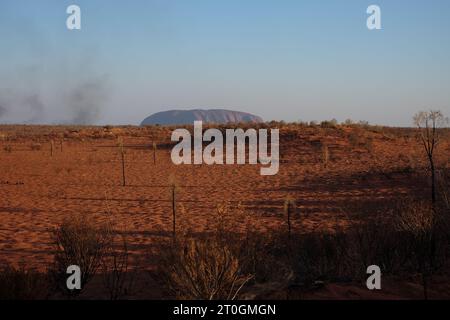 Un paysage désertique rouge, Uluru en fin d'après-midi lumière avec fumée de feu d'herbe et sable rouge, de longues ombres Banque D'Images