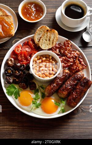 Petit-déjeuner anglais complet avec œufs frits, bacon, saucisses, haricots et champignons sur une table en bois. Banque D'Images