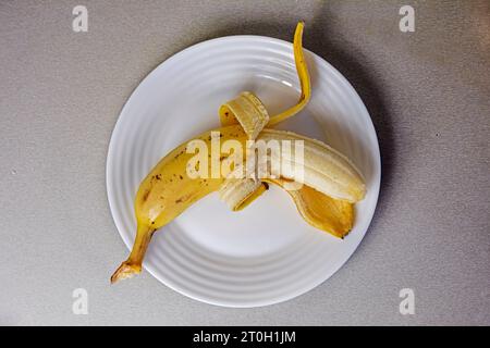 banane pelée sur une assiette blanche sur une table grise. petit déjeuner, snack Banque D'Images