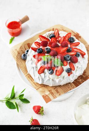 Vue de dessus de délicieux gâteau maison meringue Pavlova avec de la crème fouettée, fraises fraîches, bleuets, framboises et sauce fraise. Banque D'Images