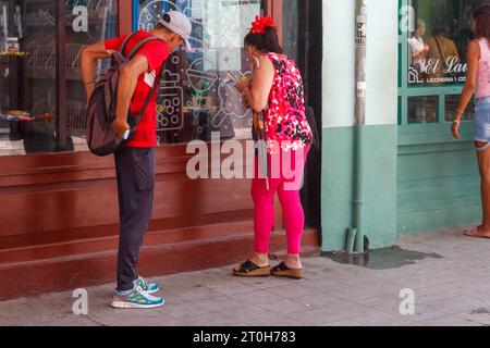 La Havane, Cuba - 29 septembre 2023 : une cubaine regarde dans une vitrine de magasin. Un homme attend à ses côtés Banque D'Images