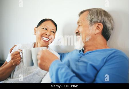 Senior, café ou couple heureux dans la chambre à coucher à la maison de liaison ou parler dans le mariage ensemble. Acclamations, boire du thé du matin ou femme asiatique riant avec un Banque D'Images