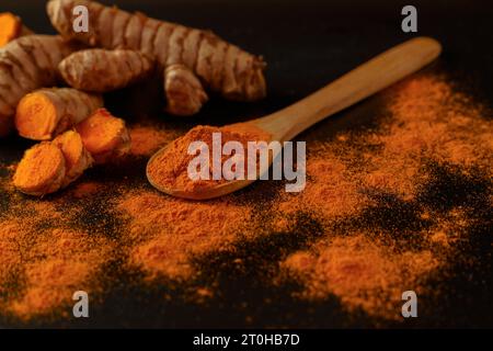 Racine de curcuma frais et curcuma moulu dans une cuillère en bois isolé sur fond noir et espace de copie Banque D'Images