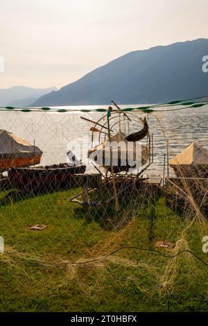 Filet de pêche avec un poisson et bateau de pêche sur le fond et le lac de Lugano avec montagne dans une journée d'été ensoleillée à Bissone, Tessin, Suisse Banque D'Images
