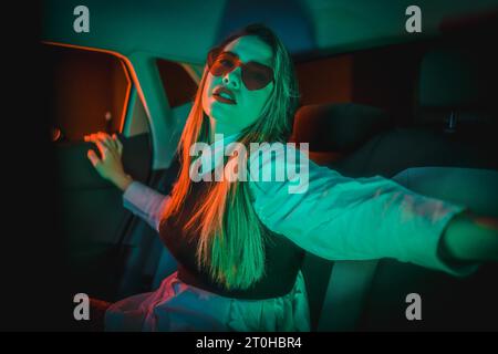 Photographie au néon à l'intérieur d'une voiture d'une jeune femme blonde caucasienne avec des lunettes de coeur Banque D'Images