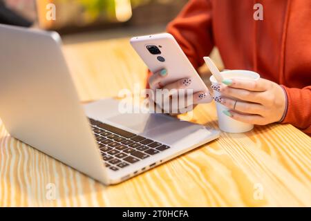 Autre personne méconnaissable avec un café chaud surfant sur Internet sur l'ordinateur et envoyant un message texte Banque D'Images