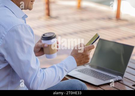 Détail des mains d'un homme latin tenant un téléphone portable devant un ordinateur portable. Banque D'Images