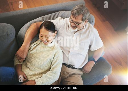 Détendez-vous, l'amour et le couple senior sur un canapé serrant, collant et s'étendant ensemble dans le salon. Heureux, sourire et vieillard homme et femme à la retraite Banque D'Images