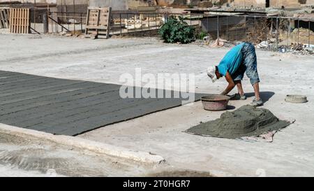 FES, Maroc - 10 septembre 2022 : artisan marocain fabriquant des tuiles avec du ciment. Il remplit le moule avec un mélange de ciment, de sable et de pigment. Banque D'Images