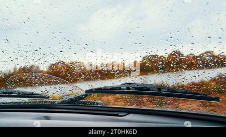 Gouttes de pluie sur le pare-brise d'une voiture. Paysage d'automne à travers un pare-brise de voiture. Mise au point sélective Banque D'Images
