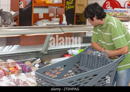 beau jeune homme, poussant un chariot dans le supermarché à la section viande et fromage sur l'allée, à la recherche de meilleurs prix Banque D'Images