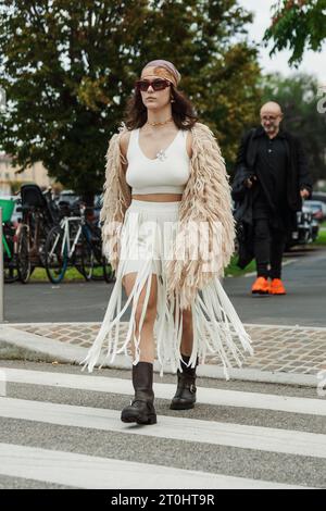 Un haut blanc invité et une jupe, manteau en maille shaggy beige, bottes noires, vu à l'extérieur du salon PRADA pendant la Fashion week de Milan vêtements pour femmes PRINTEMPS / été 2024. Banque D'Images