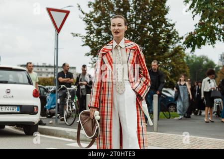 Une invitée portant un trench à carreaux, un pantalon blanc, une cravate et un sac marron, vue à l'extérieur du salon PRADA pendant la Fashion week de Milan vêtements pour femmes PRINTEMPS/été Banque D'Images