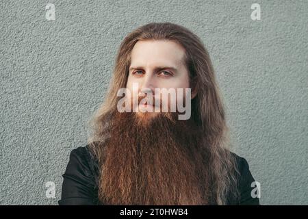 Portrait d'homme scandinave européen de trente ans longue barbe avec longue coiffure rouge lâche coiffeur sérieux avec look confiant et dents blanches en veste noire et chemise blanche. salon de coiffure Banque D'Images
