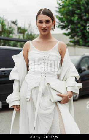 Un invité porte une robe, un manteau et un sac blancs, vus à l'extérieur du salon PRADA pendant la semaine de la mode de Milan vêtements pour femmes Printemps/été 2024. Banque D'Images