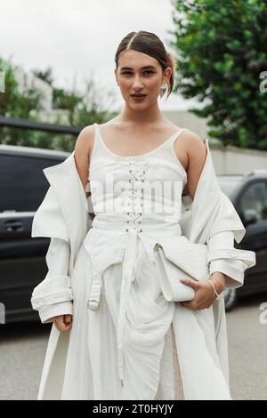 Un invité porte une robe, un manteau et un sac blancs, vus à l'extérieur du salon PRADA pendant la semaine de la mode de Milan vêtements pour femmes Printemps/été 2024. Banque D'Images